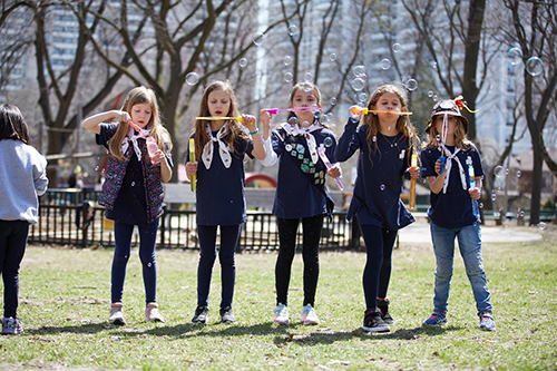 Group of girls blowing bubbles in park.