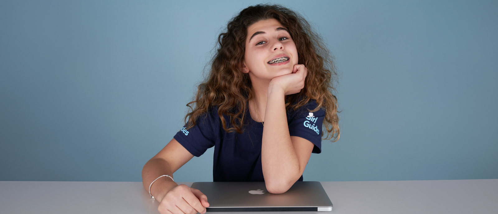Girl in uniform smiling seated in a table with a laptop