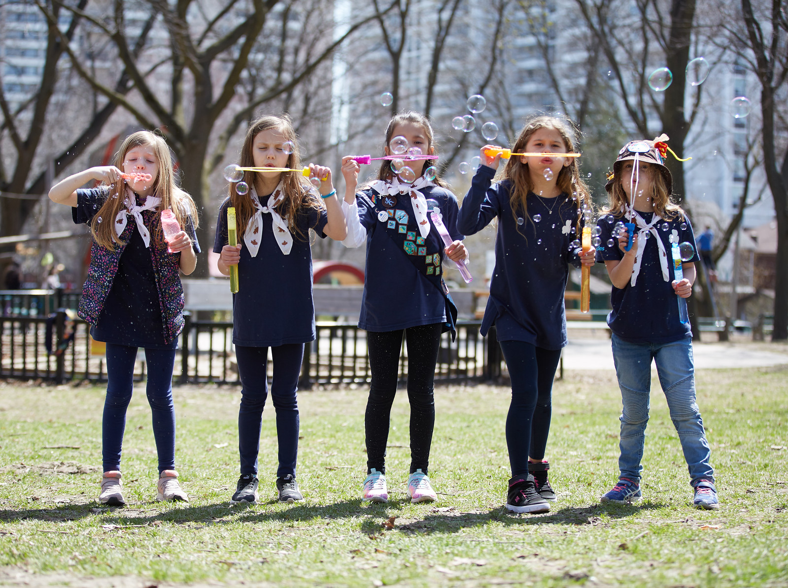 Five Girl Guides aged 7 to 8 blowing bubbles outdoors at a park