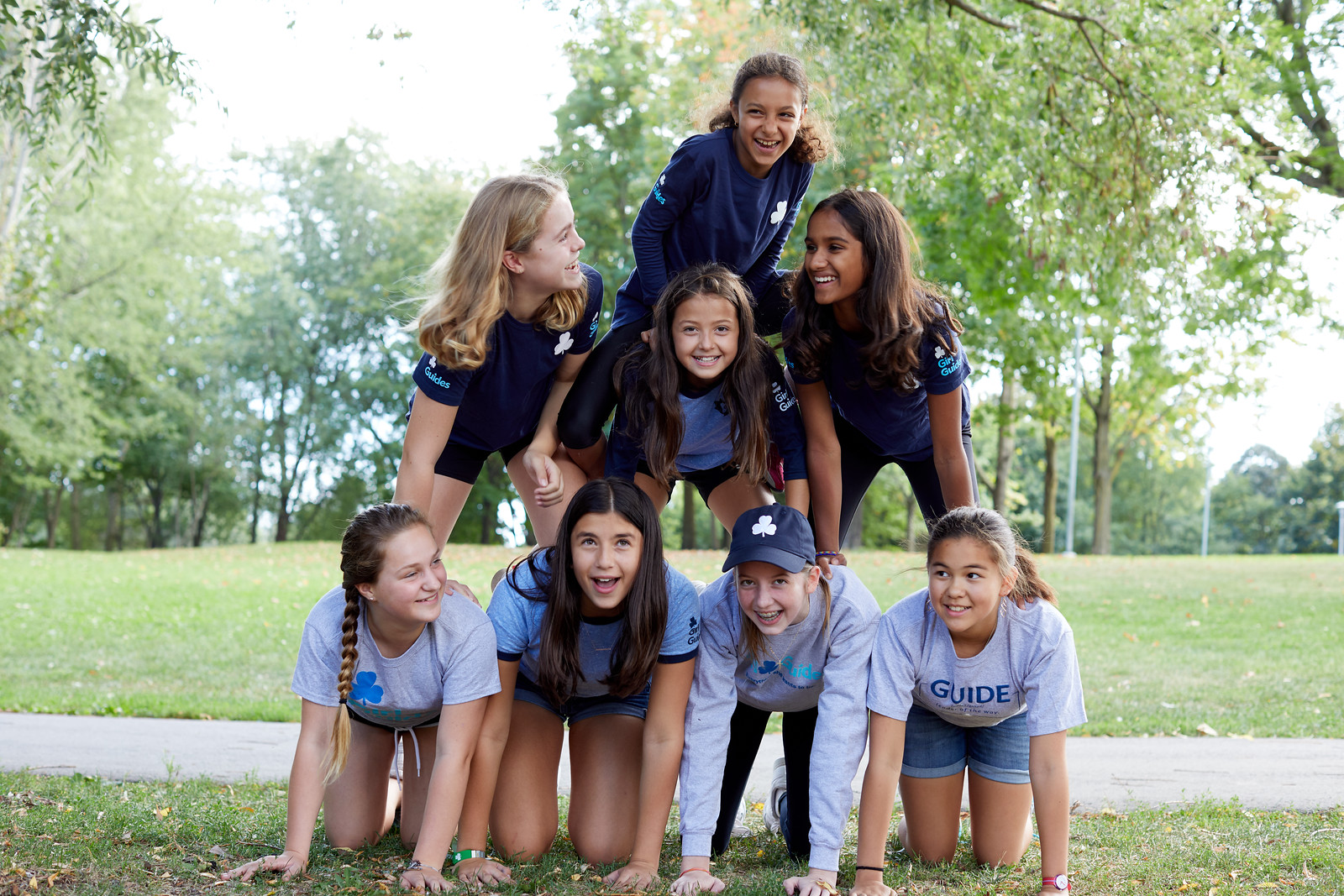 A group of Girl Guides aged 9 to 11 making a human pyramid outside in a park