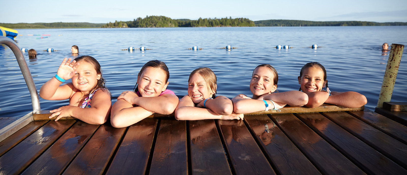 Five Girl Guides aged 9 to 11 posing on a dock at the side of a lake during a camping trip