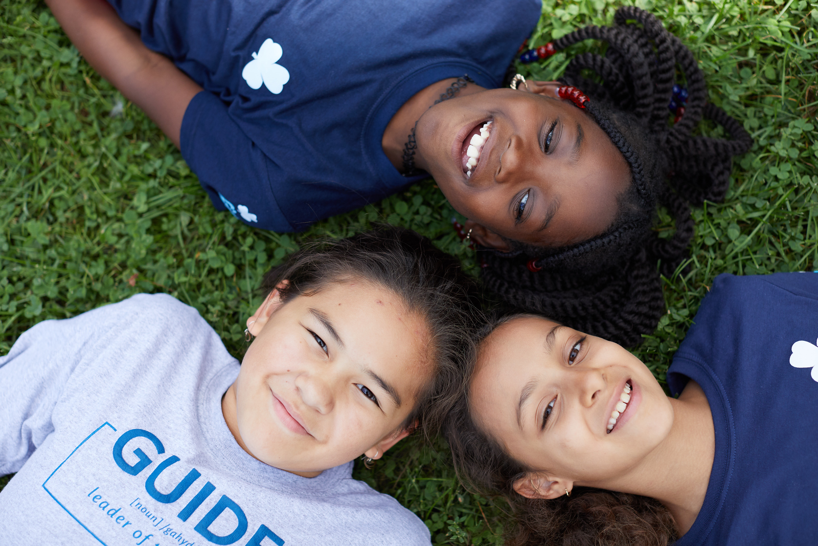 Three girls laying on the grass, smiling and enjoying a sunny day together. 